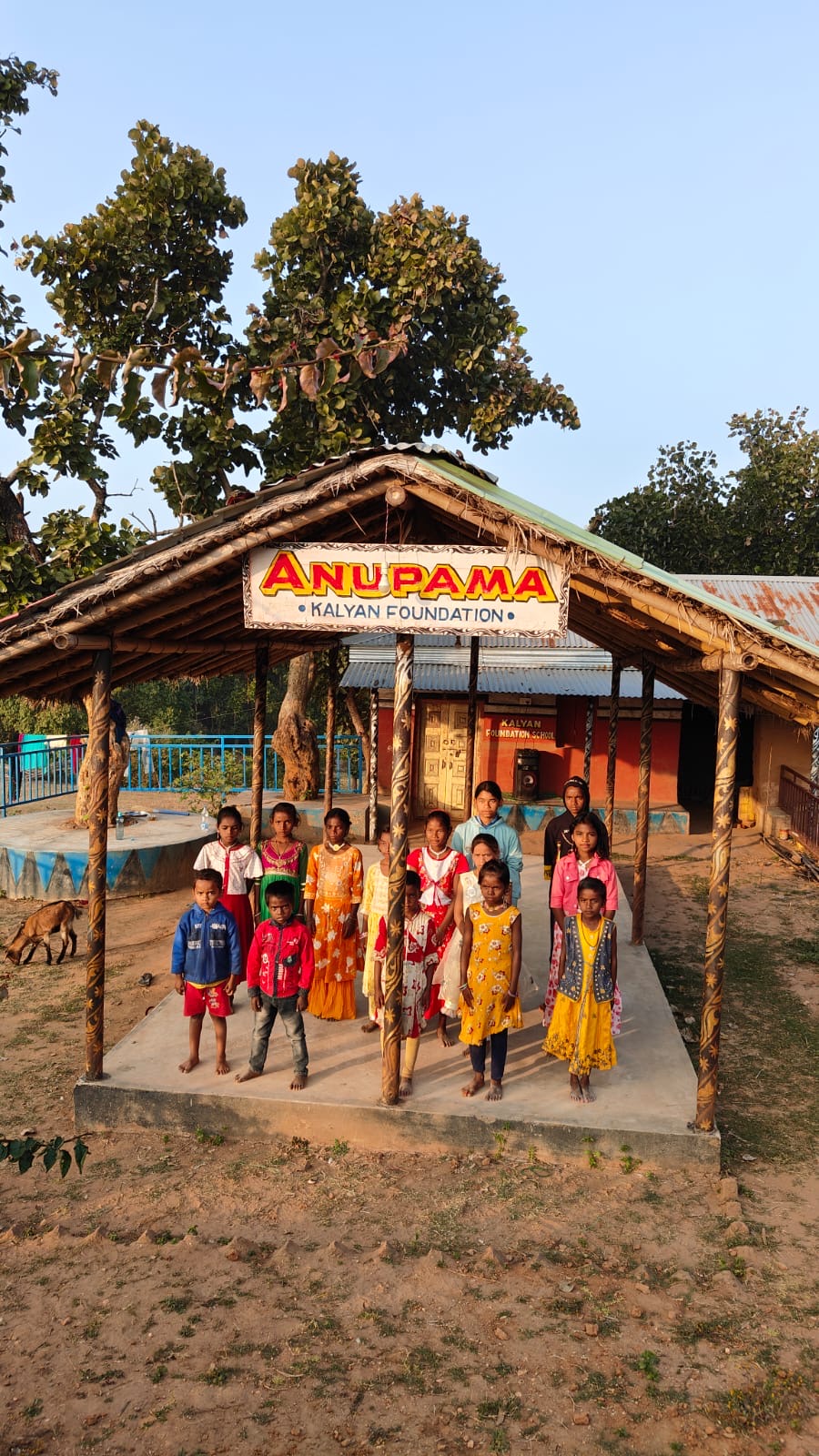 Vertical view of children standing under the Anupama Kalyan Foundation entrance with large tree above